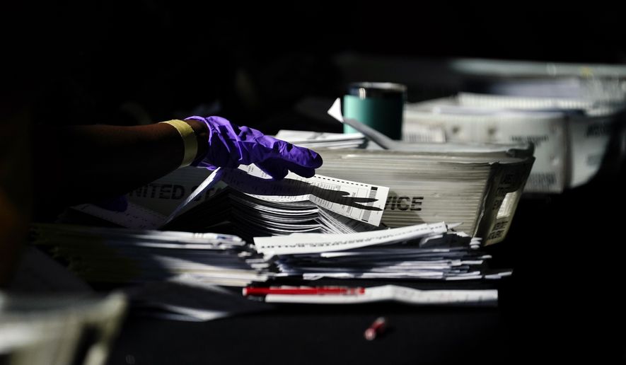 Election personnel handle ballots as vote counting in the general election continues at State Farm Arena, Wednesday, Nov. 4, 2020, in Atlanta. (AP Photo/Brynn Anderson)