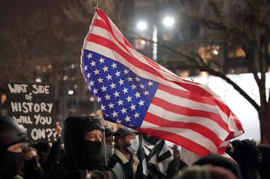 A person carries an upside down flag as people march on the night of the election in Seattle, Tuesday, Nov. 3, 2020. (AP Photo/Ted S. Warren)