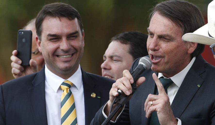 FILE - This Nov. 21, 2019 file photo shows Sen. Flavio Bolsonaro, left, with his father Brazilian President Jair Bolsonaro at the launch of his father&#39;s new political party Alliance for Brazil in Brasilia, Brazil. Public prosecutors in Rio de Janeiro state have indicted Sen. Flávio Bolsonaro for allegedly commanding a criminal organization and laundering money when he was a state lawmaker between 2007 and 2018, according to a statement the public prosecutors’ office posted to its website on Wednesday, Nov. 4, 2020. (AP Photo/Eraldo Peres, File)