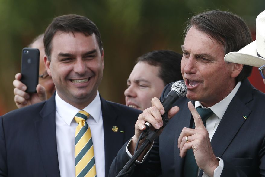 FILE - This Nov. 21, 2019 file photo shows Sen. Flavio Bolsonaro, left, with his father Brazilian President Jair Bolsonaro at the launch of his father&#39;s new political party Alliance for Brazil in Brasilia, Brazil. Public prosecutors in Rio de Janeiro state have indicted Sen. Flávio Bolsonaro for allegedly commanding a criminal organization and laundering money when he was a state lawmaker between 2007 and 2018, according to a statement the public prosecutors’ office posted to its website on Wednesday, Nov. 4, 2020. (AP Photo/Eraldo Peres, File)