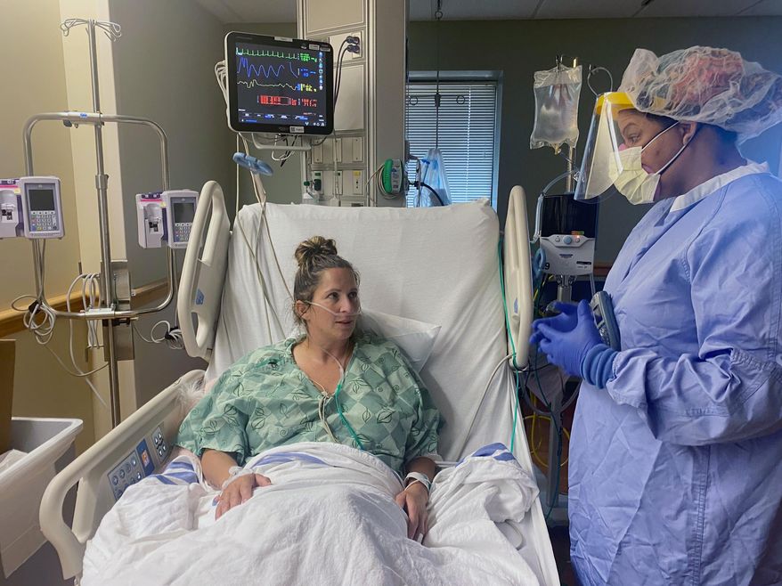 In this photo provided by Ascension Via Christi Health System, Jenifer Phelps, right, a nurse manager, talks with patient Angie Mooneyham in an intensive care unit for coronavirus patients at the Ascension Via Christi St. Francis hospital, Friday, Aug. 7, 2020 in Wichita, Kan. The hospital has created two new units for coronavirus patients as hospitalizations have increased, both in Wichita and across Kansas. (Ascension Via Christi Health System via AP)