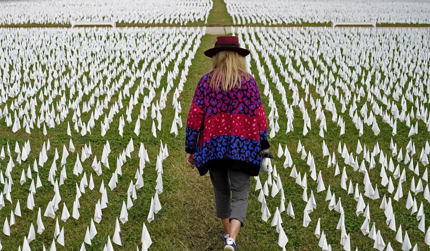 FILE - In this Oct. 27, 2020, Artist Suzanne Brennan Firstenberg walks among thousands of white flags planted in remembrance of Americans who have died of COVID-19 near Robert F. Kennedy Memorial Stadium in Washington. Regardless of the presidential election outcome, a vexing issue remains to be decided: Will the U.S. be able to tame a perilous pandemic that is surging as holidays, winter and other challenges approach? Public health experts fear the answer is no, at least in the short term, with potentially dire consequences. (AP Photo/Patrick Semansky, File)