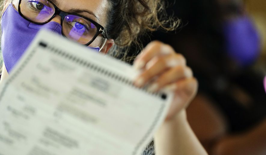 An election worker examines ballots as vote counting in the general election continues at State Farm Arena on Thursday, Nov. 5, 2020, in Atlanta. (AP Photo/Brynn Anderson)