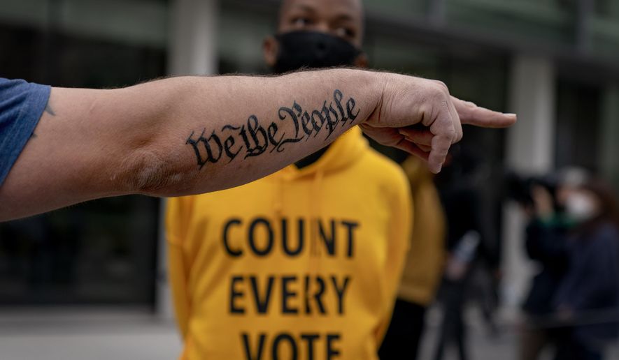 The tattoo &quot;We The People,&quot; a phrase from the United States Constitution, decorates the arm of Trump supporter Bob Lewis, left, as he argues with counter protestor Ralph Gaines while Trump supporters demonstrate against the election results outside the central counting board at the tcf Center in Detroit, Thursday, Nov. 5, 2020. (AP Photo/David Goldman)