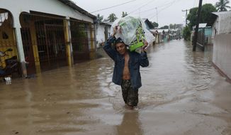 A man walks in knee-deep floodwaters carrying belongings in San Manuel, Honduras, Wednesday, Nov. 4, 2020. Eta weakened from the Category 4 hurricane to a tropical storm after lashing the Caribbean coast for much of Tuesday, its floodwaters isolating already remote communities and setting off deadly landslides. (AP Photo/Delmer Martinez)