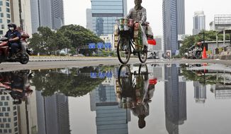 A drink vendor rides his bicycle reflected in a puddle in the main business district in Jakarta, Indonesia, Thursday, Nov. 5, 2020. Indonesia&#39;s economy entered its first recession since the Asian financial crisis more than two decades ago as the country struggles to curb the coronavirus pandemic under control. (AP Photo/Dita Alangkara)