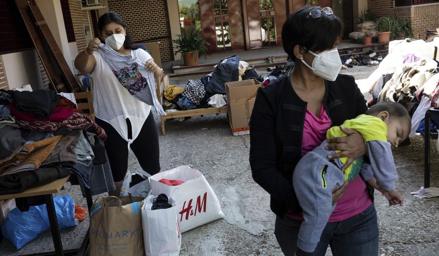 Residents of the southern neighbourhood of Vallecas pick clothes from a donation program at a Catholic parish in Madrid, Spain, Thursday, Oct. 1, 2020. Spain's government expects the economy to contract 11.2% this year, while the International Monetary Fund puts the drop at 12.8%, the highest rate among developed economies. (AP Photo/Bernat Armangue)