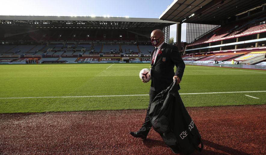 An Aston Villa member of staff wearing a mask holds a soccer ball as he walks by the pitch ahead of the English Premier League soccer match between Aston Villa and Southampton at Villa Park in Birmingham, England, Sunday, Nov. 1, 2020. The British Prime Minister Boris Johnson announced Saturday night that England will have further restrictive measures to combat the coronavirus pandemic starting Thursday, though the Premier league and other elite sport would continue. (Nick Potts via AP)