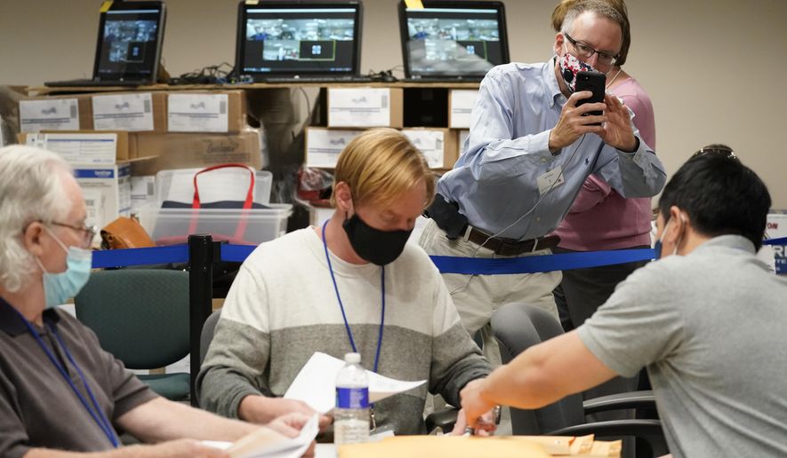 Republican canvas observer Ed White, takes photos with his smart phone as Lehigh County workers count ballots as vote counting in the general election continues, Friday, Nov. 6, 2020, in Allentown, Pa. (AP Photo/Mary Altaffer)
