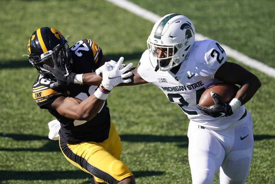 Michigan State running back Elijah Collins (24) runs from Iowa defensive back Kaevon Merriweather, left, during the first half of an NCAA college football game, Saturday, Nov. 7, 2020, in Iowa City, Iowa. (AP Photo/Charlie Neibergall)