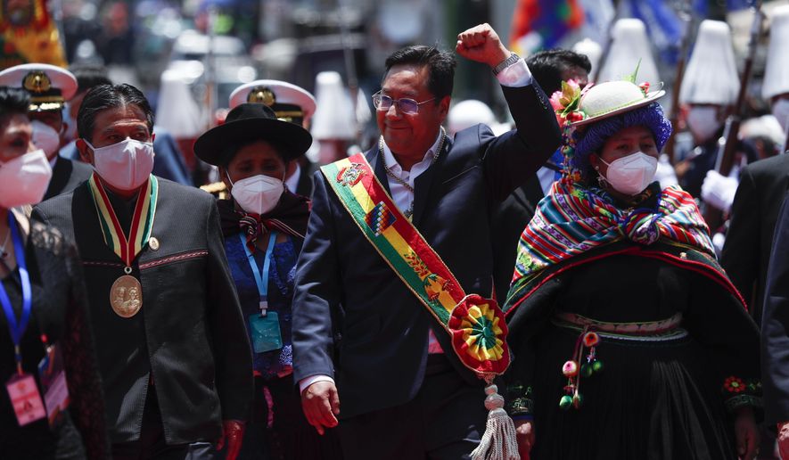 Bolivia&#39;s new President Luis Arce, center, raises his fist as he walks with Vice President David Choquehuanca, left, on their inauguration day in La Paz, Bolivia, Sunday, Nov. 8, 2020. (AP Photo/Juan Karita)
