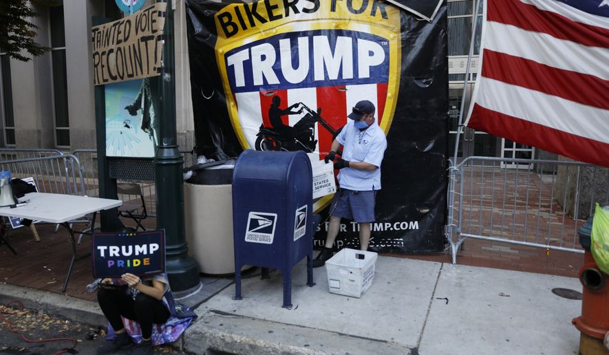 A postal worker collects mail from a mailbox inside the protest pen, as a handful of supporters of President Donald Trump continue to demonstrate, outside the Pennsylvania Convention Center in Philadelphia, Tuesday, Nov. 10, 2020. (AP Photo/Rebecca Blackwell)