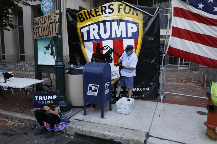 A postal worker collects mail from a mailbox inside the protest pen, as a handful of supporters of President Donald Trump continue to demonstrate, outside the Pennsylvania Convention Center in Philadelphia, Tuesday, Nov. 10, 2020. (AP Photo/Rebecca Blackwell)