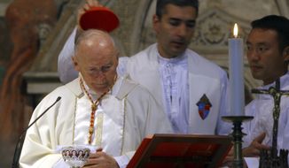 FILE - In this April 14, 2005 file photo, an aide covers the head of Washington, D.C. Cardinal Theodore McCarrick during a Mass in St. Nereus and Achilleus Church in Rome. On Tuesday, Nov. 10, 2020, the Vatican is taking the extraordinary step of publishing its two-year investigation into the disgraced ex-Cardinal McCarrick, who was defrocked in 2019 after the Vatican determined that years of rumors that he was a sexual predator were true. (AP Photo/ Alessandra Tarantino, File)