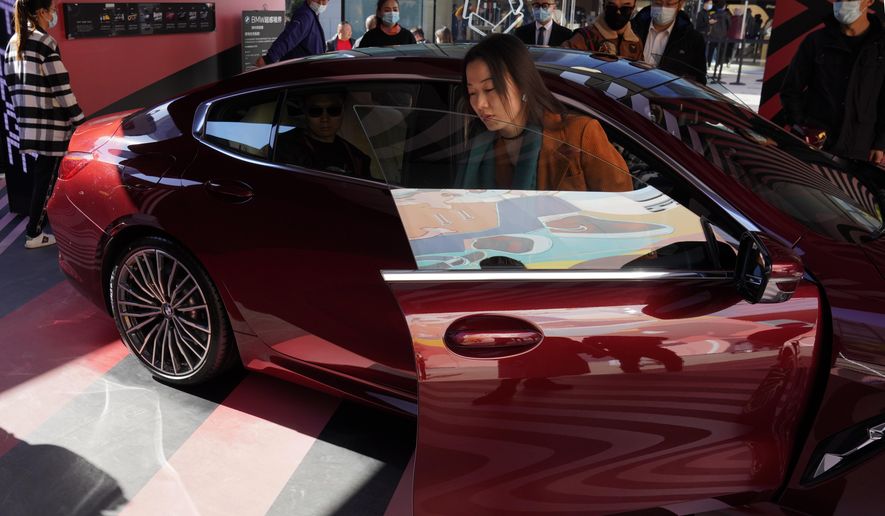 A woman exits a car on display during a promotion held in a popular shopping district in Beijing on Sunday, Nov. 8, 2020. China's sales of vehicles including trucks and buses rose 12.5% over a year earlier in October as the industry recovered from the coronavirus, but total purchases in the year's first 10 months still were below pre-virus levels, an industry group reported Wednesday, Nov. 11, 2020. (AP Photo/Ng Han Guan)