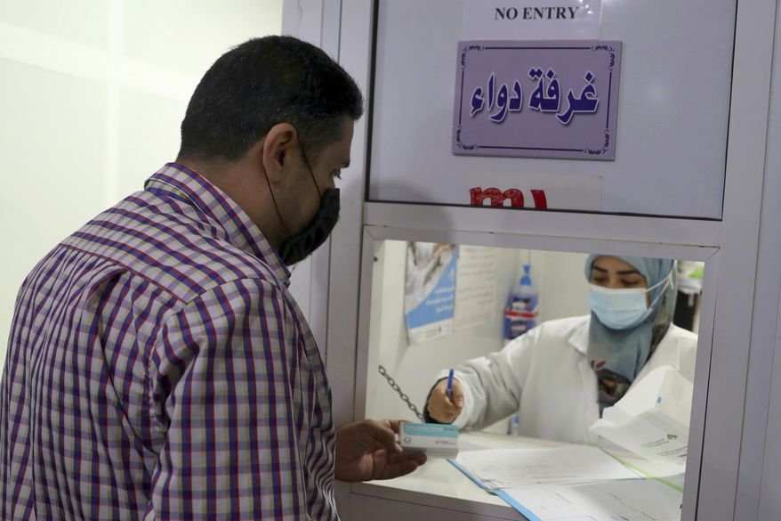 Hassan Taha, who suffers from a heart condition, receives medication from a pharmacist at the Amel Association, a Lebanese humanitarian group, in Dahiyeh, a southern suburb of Beirut, Lebanon, Tuesday, Nov. 3, 2020. Lebanese have been forced to search far and wide for their prescriptions after many medications vanished from pharmacies. It's the latest chapter in their country's financial breakdown. (AP Photo/Bilal Hussein)