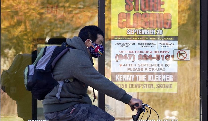 FILE - In this Friday, Nov. 6, 2020 file photo, a man wearing a face mask rides a bicycle past a closed store in Wilmette, Ill. The state set another single-day record for coronavirus infections Tuesday, Nov. 10, 2020, pushing the total number of people who have tested positive for the virus in the state since the pandemic began past 500,000. (AP Photo/Nam Y. Huh)