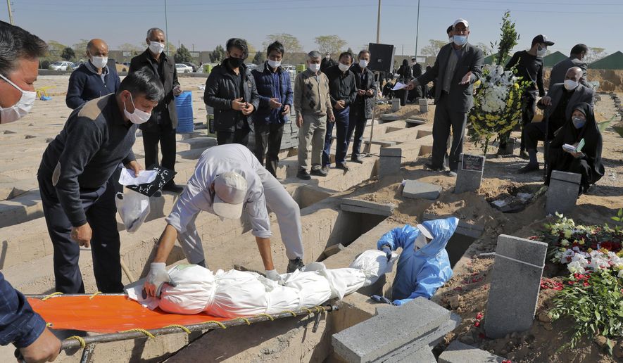 The body of a person who died from COVID-19 is interred as mourner look on, at the Behesht-e-Zahra cemetery on the outskirts of Tehran, Iran, Sunday, Nov. 1, 2020. The cemetery is struggling to keep up with the coronavirus pandemic ravaging Iran, with double the usual number of bodies arriving each day and grave diggers excavating thousands of new plots. (AP Photo/Ebrahim Noroozi)