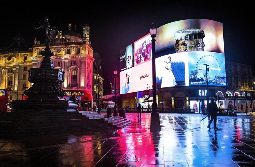 A man walks across the normally busy Piccadilly Circus in central London after a heavy rain downpour, Monday Nov. 9, 2020. The London streets are nearly deserted during the first full week of a four-week coronavirus lockdown in England, but some are calling to allow businesses to reopen their doors to kickstart the city economy. (Victoria Jones/PA via AP)