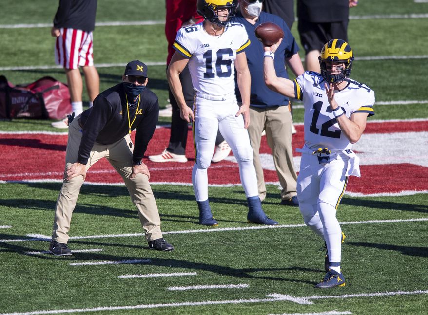 Michigan head coach Jim Harbaugh, left, watches as quarterback Cade McNamara (12) warms up before an NCAA college football game against Indiana, Saturday, Nov. 7, 2020, in Bloomington, Ind. (AP Photo/Doug McSchooler)
