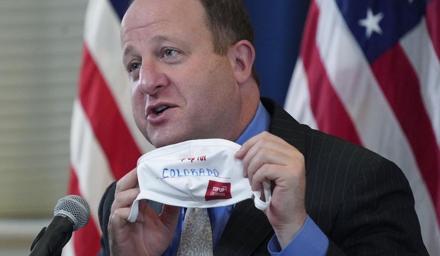FILE - In this Oct. 20, 2020, file photo, Colorado Gov. Jared Polis holds up a face mask featuring the state's new advertising campaign to encourage residents to protect against COVID-19 during a news conference in Denver. Polis is telling lawmakers his $35 billion budget request for the next fiscal year aims to ease residents' suffering this winter because of the coronavirus and position the state for a long-term post-pandemic recovery. (AP Photo/David Zalubowski, File)