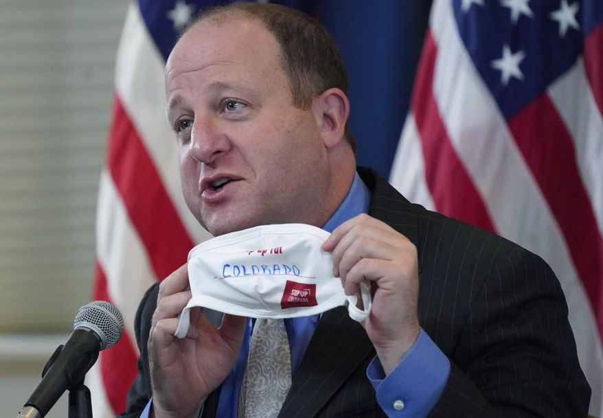 FILE - In this Oct. 20, 2020, file photo, Colorado Gov. Jared Polis holds up a face mask featuring the state's new advertising campaign to encourage residents to protect against COVID-19 during a news conference in Denver. Polis is telling lawmakers his $35 billion budget request for the next fiscal year aims to ease residents' suffering this winter because of the coronavirus and position the state for a long-term post-pandemic recovery. (AP Photo/David Zalubowski, File)