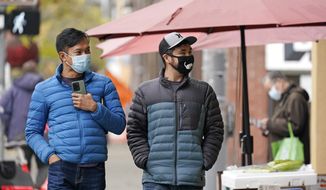 Pedestrians wearing masks walk past a small grocery store in the Chinatown-International District Thursday, Nov. 12, 2020, in Seattle. Washington state and county health officials have warned of a spike in coronavirus cases across the state, and pleaded with the public to take the pandemic more seriously heading into the winter holidays. (AP Photo/Elaine Thompson)