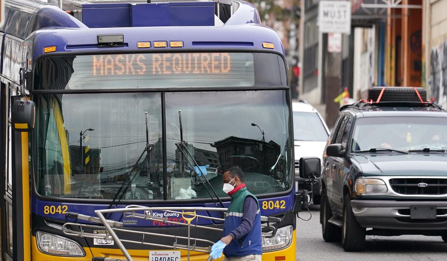 A Metro bus driver wears a mask as he walks past his coach and beneath a "masks required" sign Thursday, Nov. 12, 2020, in Seattle. Washington state and county health officials have warned of a spike in coronavirus cases across the state, and pleaded with the public to take the pandemic more seriously heading into the winter holidays. (AP Photo/Elaine Thompson)