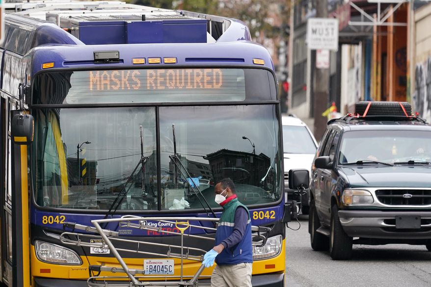 A Metro bus driver wears a mask as he walks past his coach and beneath a "masks required" sign Thursday, Nov. 12, 2020, in Seattle. Washington state and county health officials have warned of a spike in coronavirus cases across the state, and pleaded with the public to take the pandemic more seriously heading into the winter holidays. (AP Photo/Elaine Thompson)