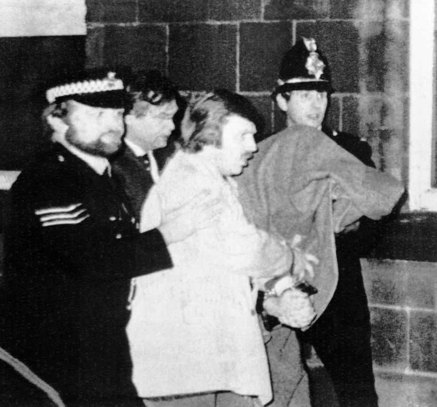 This Jan. 5, 1981 file photo shows Peter William Sutcliffe, 35, under a blanket at right, being led from Dewsbury Magistrates Court in Dewsbury by police officers. On Friday, Nov. 13, 2020, Britain’s Prison Service said that serial killer Peter Sutcliffe, known as the "Yorkshire Ripper", died in the hospital. Sutcliffe was serving a life sentence after being convicted of murdering 13 women in northern England between 1975 and 1980. (AP Photo/Pyne, file)