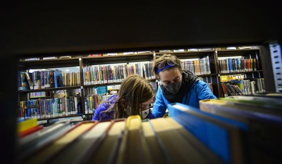 Beatrix Robb, 13, of Brattleboro, Vt., and her mother, Jen, look for a book at the Brooks Memorial Library, in Brattleboro, Vt., Friday, Nov. 13, 2020. The library plans to close its doors on Thanksgiving and reopen on Dec. 14, 2020, as the number of COVID-19 cases are on the rise in the area. (Kristopher Radder/The Brattleboro Reformer via AP)