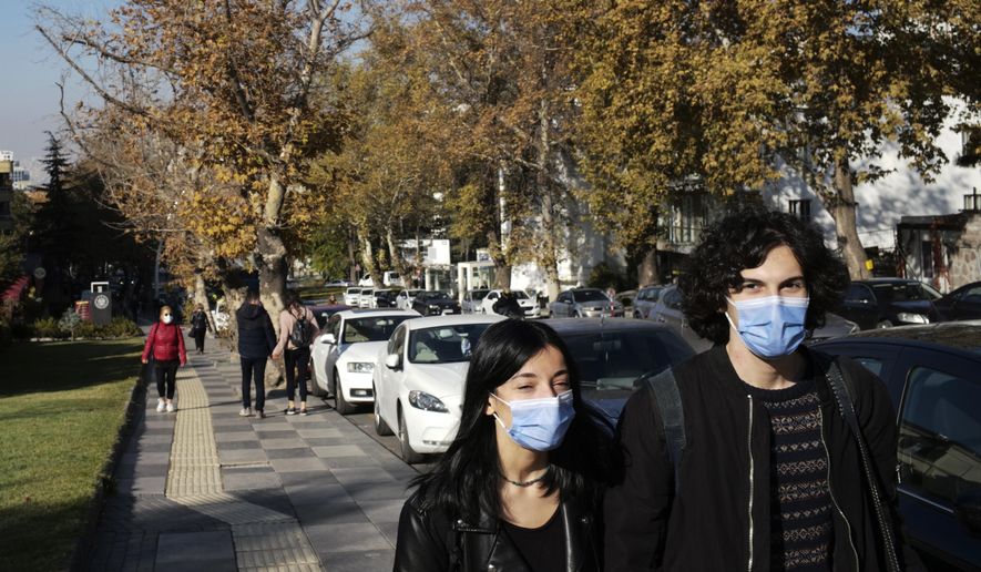 People wearing masks to help protect against the spread of coronavirus, walk along a public garden, in Ankara, Turkey, Friday, Nov. 13, 2020. Turkey's interior ministry has banned smoking in public places, including parks, across the country to curb the spread of COVID-19. (AP Photo/Burhan Ozbilici)