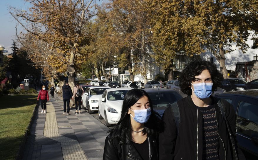 People wearing masks to help protect against the spread of coronavirus, walk along a public garden, in Ankara, Turkey, Friday, Nov. 13, 2020. Turkey's interior ministry has banned smoking in public places, including parks, across the country to curb the spread of COVID-19. (AP Photo/Burhan Ozbilici)