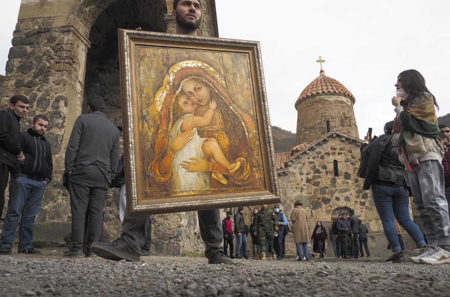 A man holds an icon from the Dadivank, an Armenian Apostolic Church monastery dating to the 9th century, as ethnic Armenians leave the separatist region of Nagorno-Karabakh to Armenia, Saturday, Nov. 14, 2020. The territory is to be turned over to Azerbaijan on Sunday as part of territorial concessions in an agreement to end six weeks of intense fighting with Armenian forces. Hundreds of thousands of Azeris were displaced by the war that ended in 1994. It is unclear when any civilians might try to settle in Karvachar — which will now be known by its Azeri name Kalbajar — or elsewhere. (AP Photo/Dmitry Lovetsky)