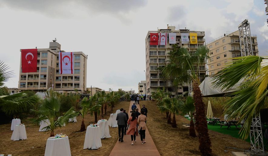 People walk at the decorates side in front of the abandoned buildings with a Turkish and Turkish Cypriots breakaway flags, before Turkish President Recep Tayyip Erdogan inspects the newly opened beachfront of Varosha in war-divided Cyprus&#39; in the Turkish occupied area in the breakaway Turkish Cypriot north on Sunday, Nov. 15, 2020. Erdogan appeared to throw a fresh bid to restart dormant Cyprus reunification talks into doubt, saying that a two-state deal rather than the long-established federal formula is the way forward. (AP Photo/Nedim Enginsoy)