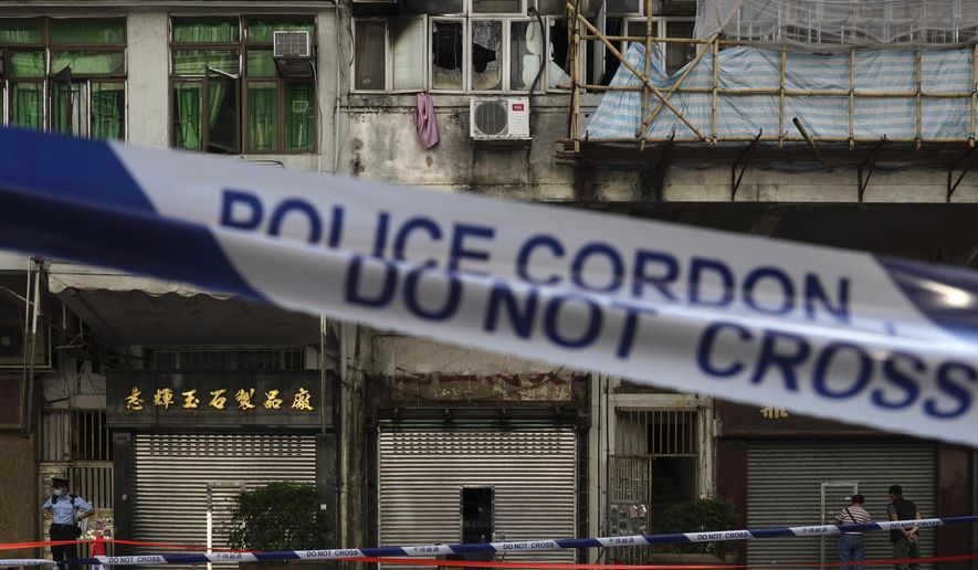 A police cordon line is set at a fire site, top center with broken windows, in Hong Kong Monday, Nov. 16, 2020. City authorities said a fire in a crowded residential district in Hong Kong has "caused a number of deaths and injuries". (AP Photo/Vincent Yu)