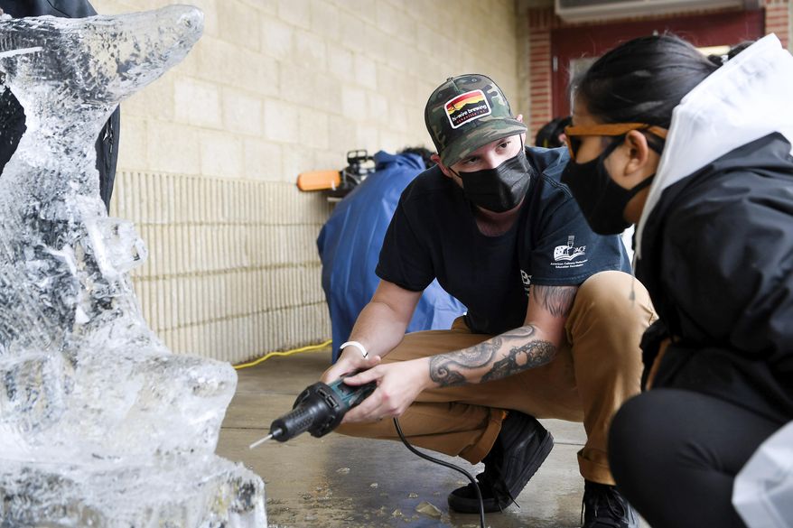 AB Tech teaching chef Chris Bugher helps Yu Nanda Maung with a carving technique as she sculpts a shark from a block of ice on Nov. 10, 2020, at Asheville–Buncombe Technical Community College in Ashville, N.C. (Angela Wilhelm/The Asheville Citizen-Times via AP)