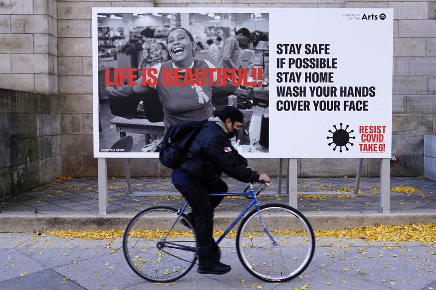 A man wearing a face mask bicycles along Broad Street, Wednesday, Nov. 18, 2020, in Philadelphia. Pennsylvania is strengthening its mask mandate and will require out-of-state travelers to test negative for the coronavirus before arrival, health officials announced Tuesday, taking additional steps to address a sharp increase in infections and hospitalizations. (AP Photo/Matt Slocum)