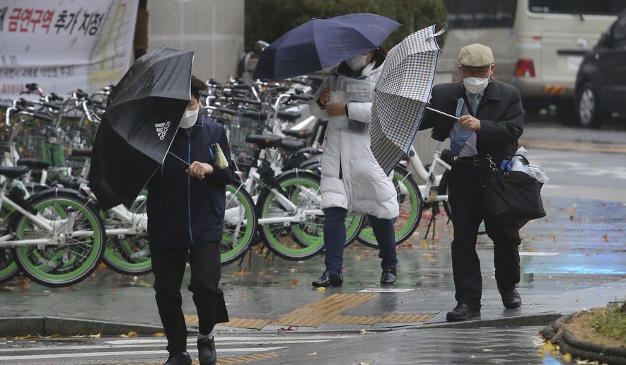 People wearing face masks to help protect against the spread of the coronavirus try to manage their umbrellas in the rain in Seoul, South Korea, Thursday, Nov. 19, 2020. South Korea has reported more than 300 new coronavirus cases for a second consecutive day as authorities begin enforcing toughened social distancing rules in some areas to fight a resurgence of small-scale clusters of infections. (AP Photo/Ahn Young-joon)