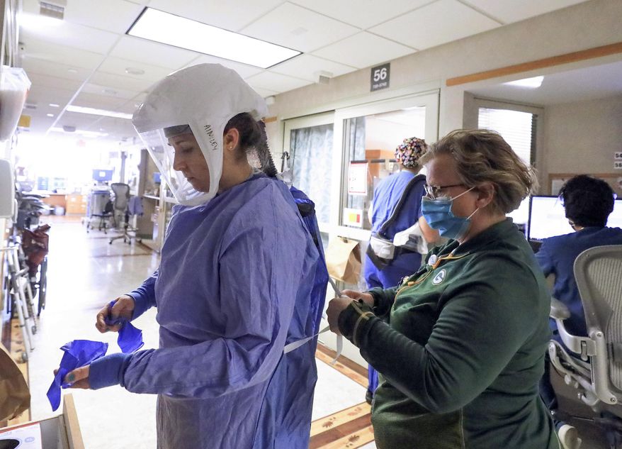 FILE - In this Nov. 5, 2020, file photo, Deb Dalsing, nurse manager of the COVID-19 treatment unit at UW Health assists nurse Ainsley Billesbach with her personal protective equipment at the hospital in Madison, Wis. Conditions inside the nation’s hospitals are deteriorating by the day as the coronavirus rages through the country at an unrelenting pace. (John Hart/Wisconsin State Journal via AP)