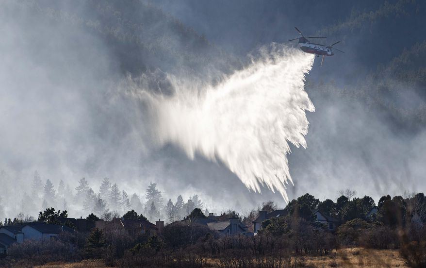 A Chinook helicopter drops water on a wildfire near Bear Creek Regional Park on the westside of Colorado Springs, Colo., Thursday, Nov. 19, 2020. About 235 homes were evacuated near the park as firefighters battled the fire on the ground and in the air. (Christian Murdock/The Gazette via AP)