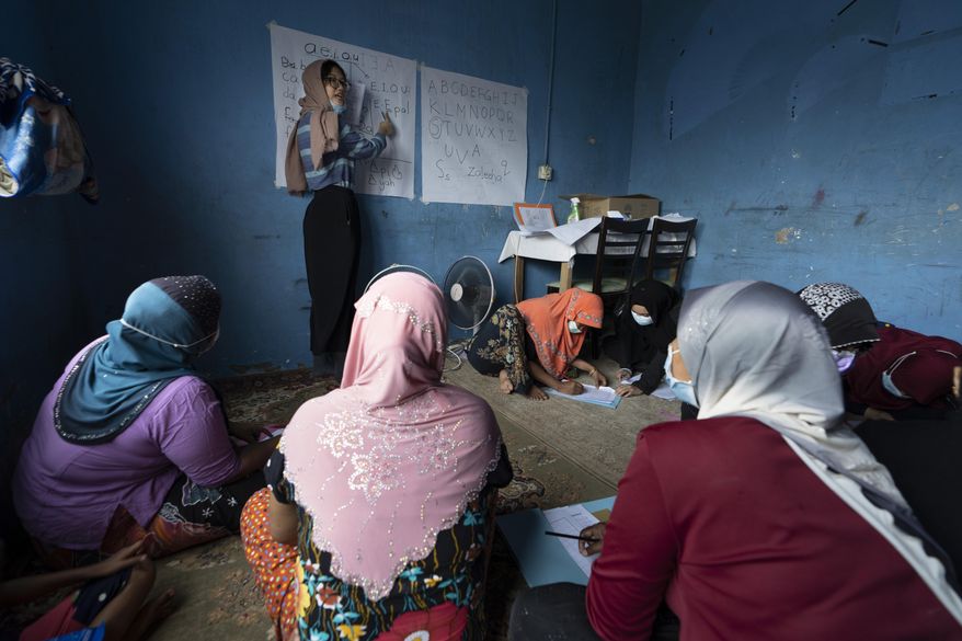 A volunteer teacher gives a basic English lesson to a minority Muslim Rohingya refugees at a slum on the outskirts of Kuala Lumpur, Malaysia, on Oct. 11, 2020. Refugee women in Malaysia, some in their late 50s, are learning to read and write for the first time. The classes outside Kuala Lumpur are offered by the Women for Refugees group, which was formed in September by two law students to help illiterate migrant women integrate into the local community and empower them to be more than just passive wives. (AP Photo/Vincent Thian)