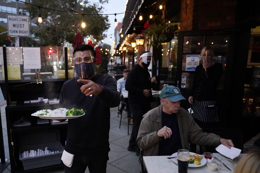 A server carries food for a customer at Ye Olde King's Head on Thursday, Nov. 19, 2020, in Santa Monica, Calif. The British restaurant and bar in seaside Southern California has been battered the past nine months and was in the process of adapting to new restrictions that took effect Friday, Nov. 20 that would further crimp its recovery even as the prospect of a crippling shutdown loomed.  (AP Photo/Marcio Jose Sanchez)