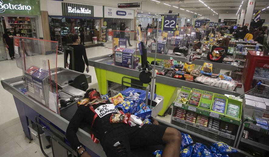 Jonata Anjo lies on a checkout counter at a Carrefour supermarket during a protest against the murder of Black man Joao Alberto Silveira Freitas at a different Carrefour supermarket the night before, on Brazil's National Black Consciousness Day in Rio de Janeiro, Brazil, Friday, Nov. 20, 2020. Freitas died after being beaten by supermarket security guards in the southern Brazilian city of Porto Alegre, sparking outrage as videos of the incident circulated on social media. (AP Photo/Bruna Prado)