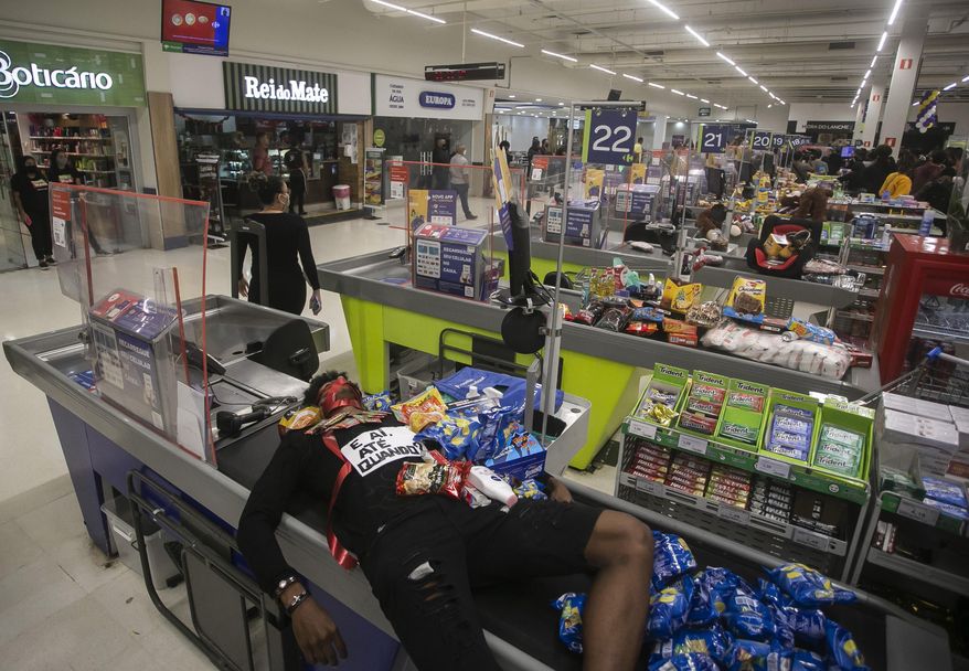 Jonata Anjo lies on a checkout counter at a Carrefour supermarket during a protest against the murder of Black man Joao Alberto Silveira Freitas at a different Carrefour supermarket the night before, on Brazil's National Black Consciousness Day in Rio de Janeiro, Brazil, Friday, Nov. 20, 2020. Freitas died after being beaten by supermarket security guards in the southern Brazilian city of Porto Alegre, sparking outrage as videos of the incident circulated on social media. (AP Photo/Bruna Prado)