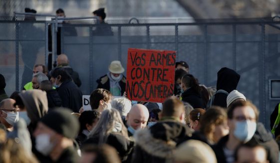 Demonstrators gather during a protest against bill on police images, in Paris, Saturday, Nov. 21, 2020. Thousands of people took to the streets in Paris and other French cities Saturday to protest a proposed security law they say would impinge on freedom of information and media rights. The board reads: Your guns against our cameras. (AP Photo/Christophe Ena)