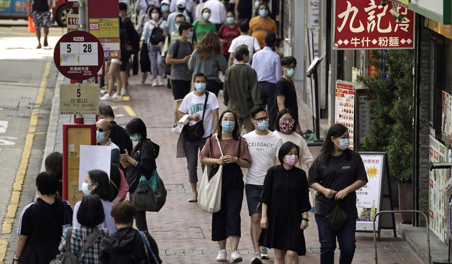 In this Oct. 9, 2020, file photo, people wearing masks to protect against the coronavirus, walk down a street in Hong Kong. Singapore and Hong Kong have postponed a planned air travel bubble meant to boost tourism for both cities, amid a spike in coronavirus infections in Hong Kong. The air travel bubble, originally slated to begin Sunday, will be delayed by at least two weeks, Hong Kong’s minister of commerce and economic development, Edward Yau, said at a news conference on Saturday, Nov. 21, 2020. (AP Photo/Kin Cheung, File)