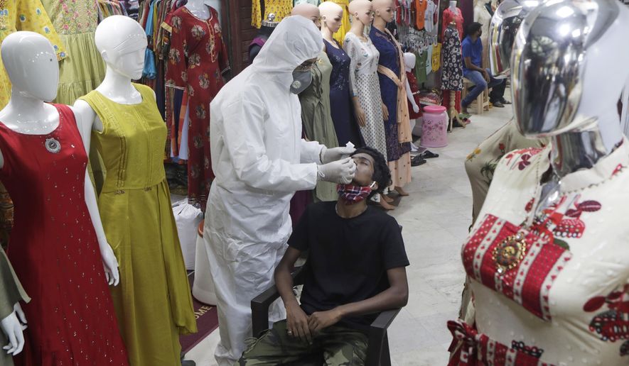A health worker takes a swab sample to test for COVID-19 inside a garment market in Mumbai, India, Friday, Nov. 20, 2020. India’s total number of coronavirus cases since the pandemic began crossed 9 million on Friday. (AP Photo/Rajanish Kakade)