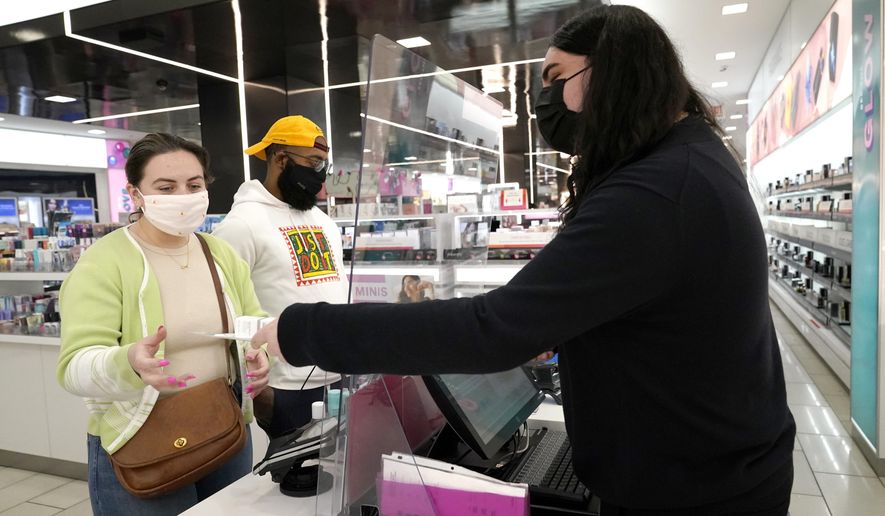 Cashier Druhan Parker, right, works behind a plexiglass shield Thursday, Nov. 19, 2020, as he checks out shoppers Cassie Howard, left, and Paris Black at an in Chicago. The accelerating surge of coronavirus cases across the U.S. is causing an existential crisis for America’s retailers and spooking their customers just as the critically important holiday shopping season nears. (AP Photo/Charles Rex Arbogast)