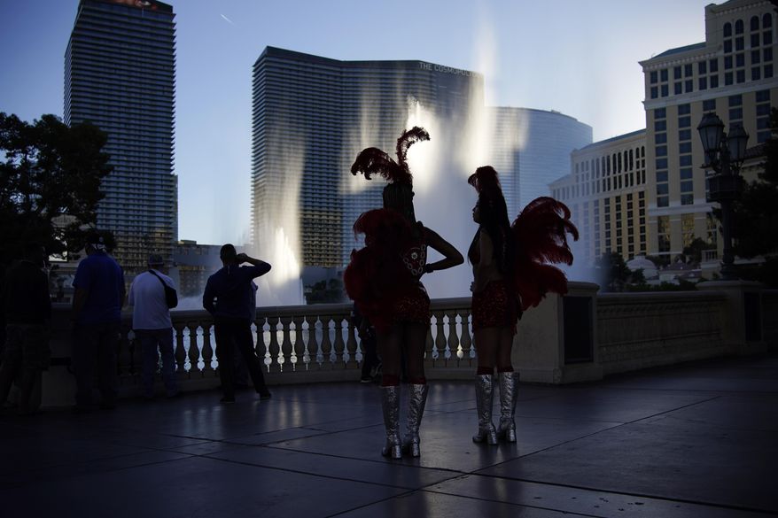 People dressed as showgirls stand along the Las Vegas Strip, Thursday, Nov. 19, 2020, in Las Vegas. As the coronavirus surges to record levels in Nevada, the governor has implored residents to stay home. But Democrat Steve Sisolak has also encouraged out-of-state visitors, the lifeblood of Nevada&#x27;s limping economy, to come to his state and spend money in Las Vegas. (AP Photo/John Locher)